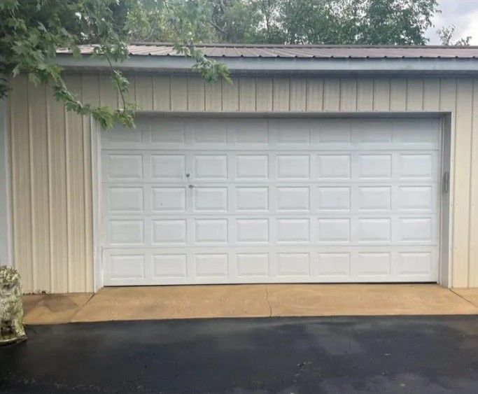 White double garage door on a tan metal building, with wet pavement in front.