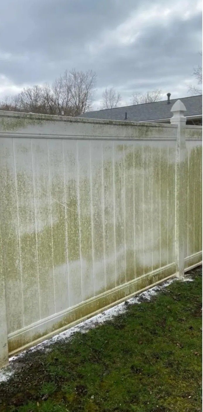 Snow-covered white fence beside a grassy yard under a cloudy sky