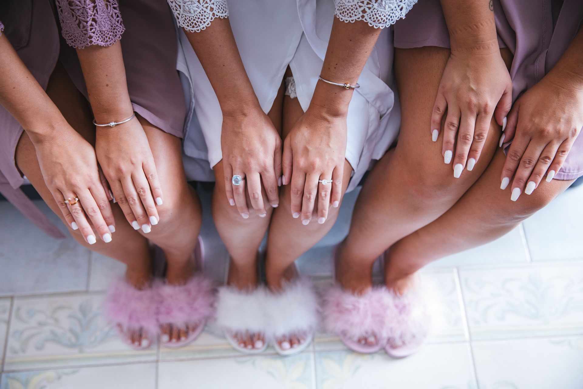 Four people sitting on a tile floor wearing matching robes and fluffy slippers, resting their hands on their knees.