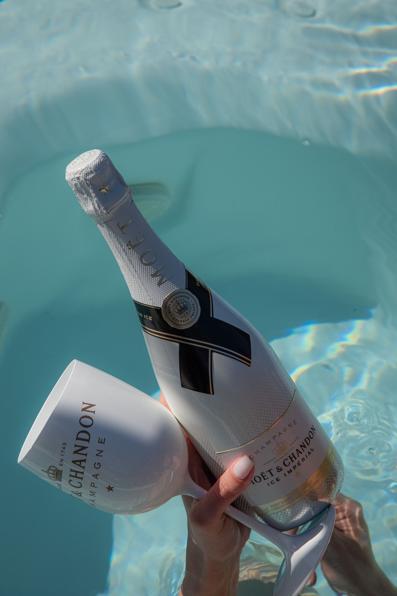 Una persona tiene in mano una bottiglia e un bicchiere di Chandon in una piscina turchese.