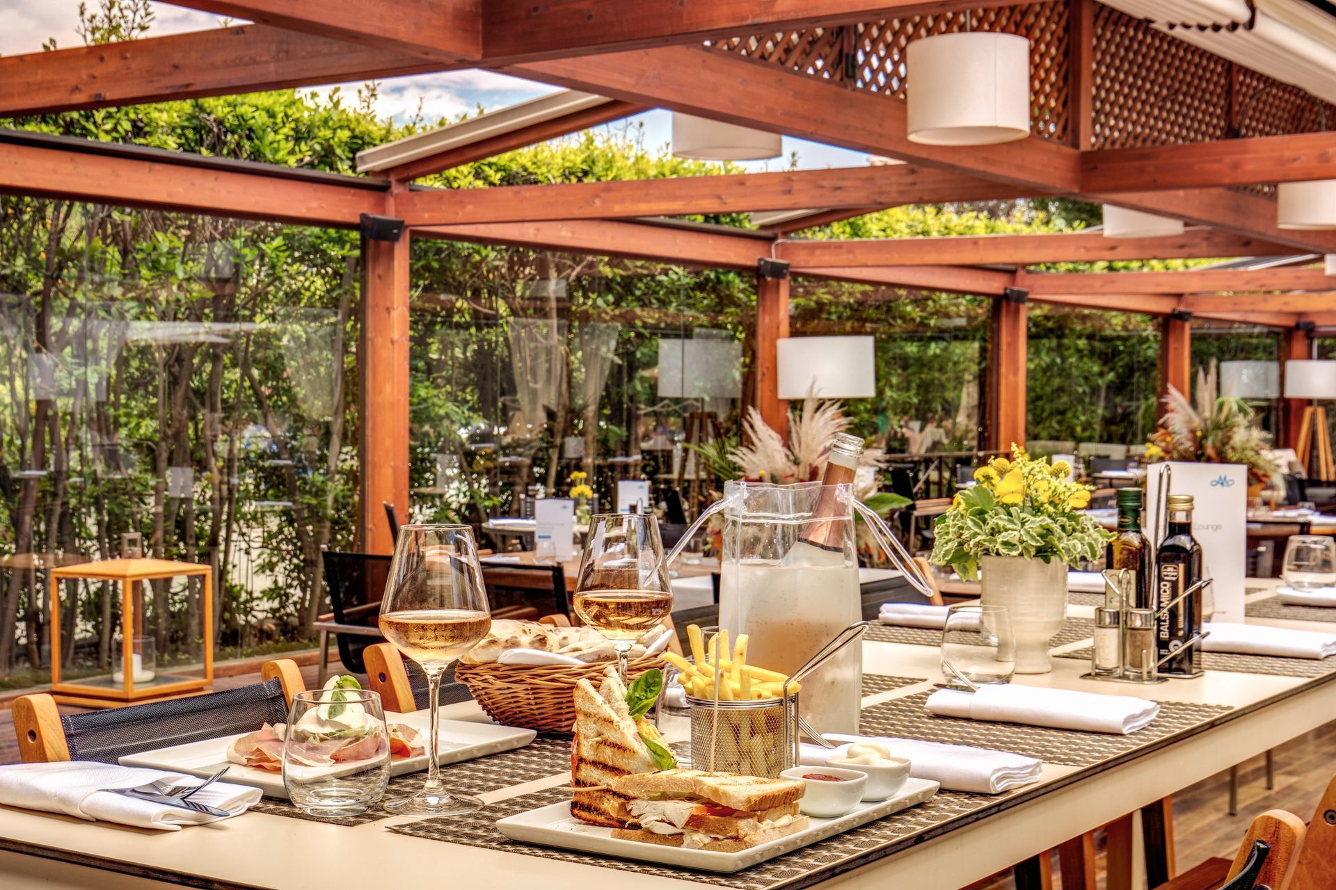 Outdoor buffet table under a wooden pergola with flowers, candles, and neatly arranged dishes.