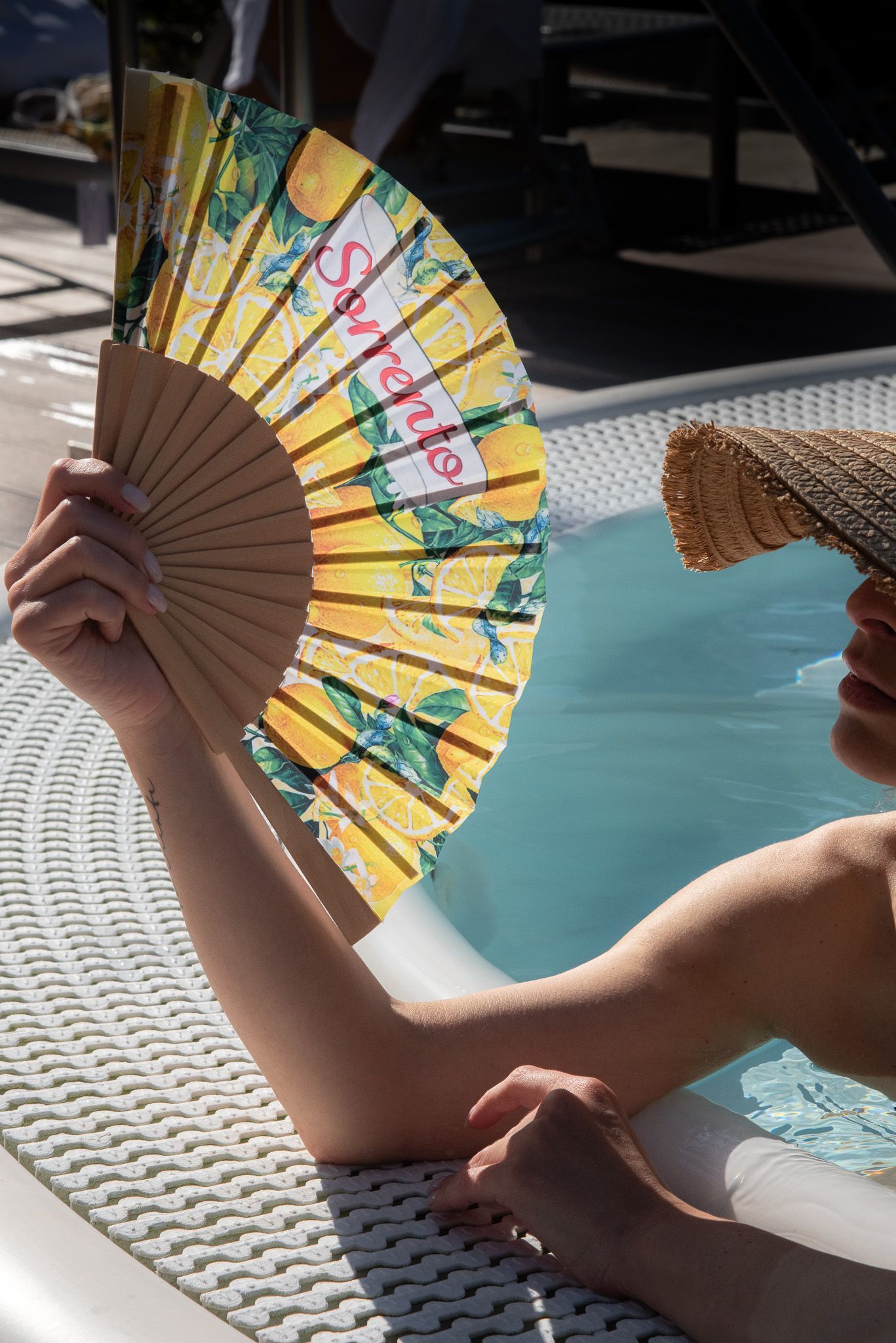 Una persona in piscina tiene in mano un ventaglio giallo con decorazioni a limoni e la scritta 