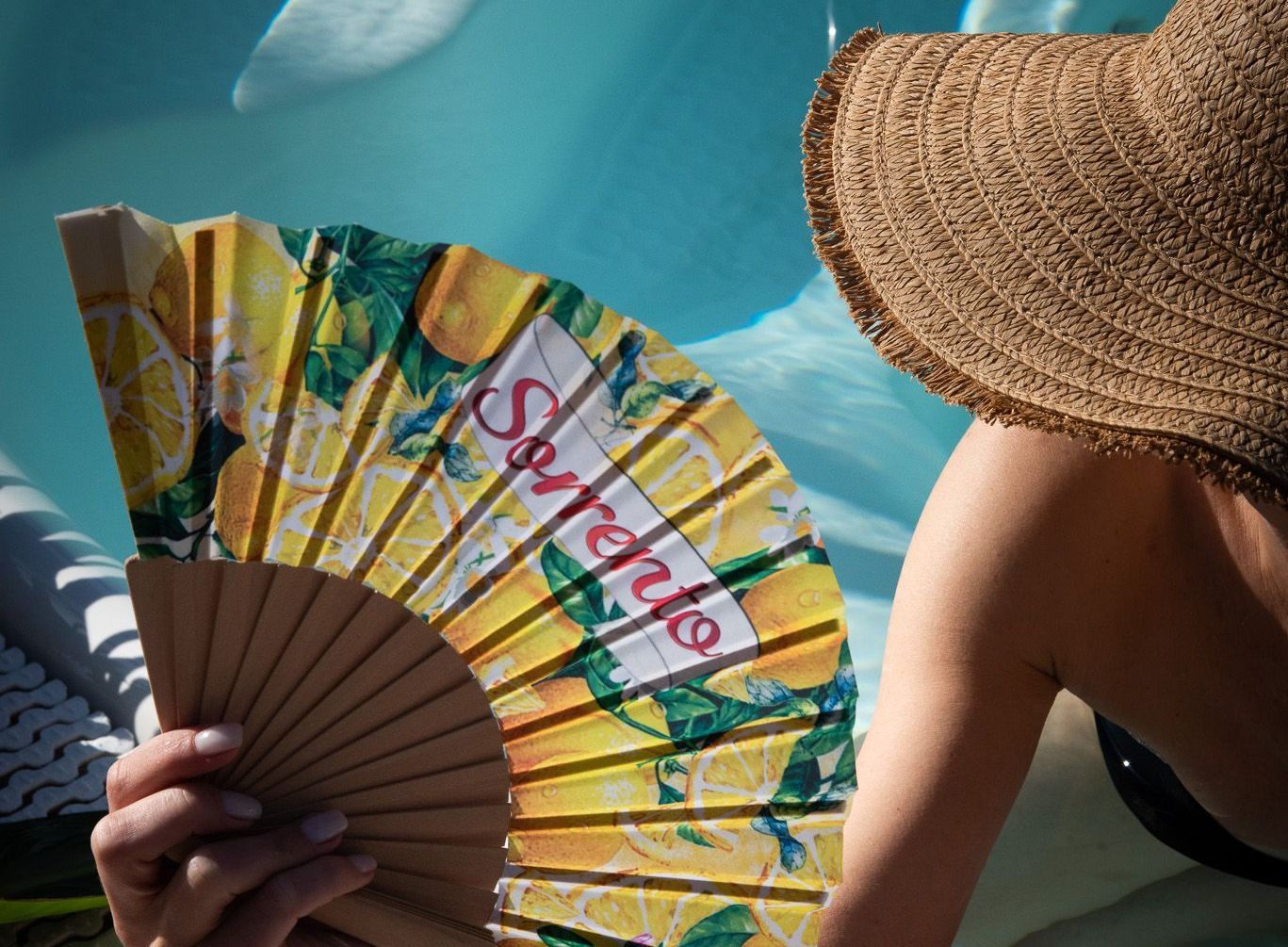 A person wearing a straw hat holds a yellow folding fan with a lemon print and 
