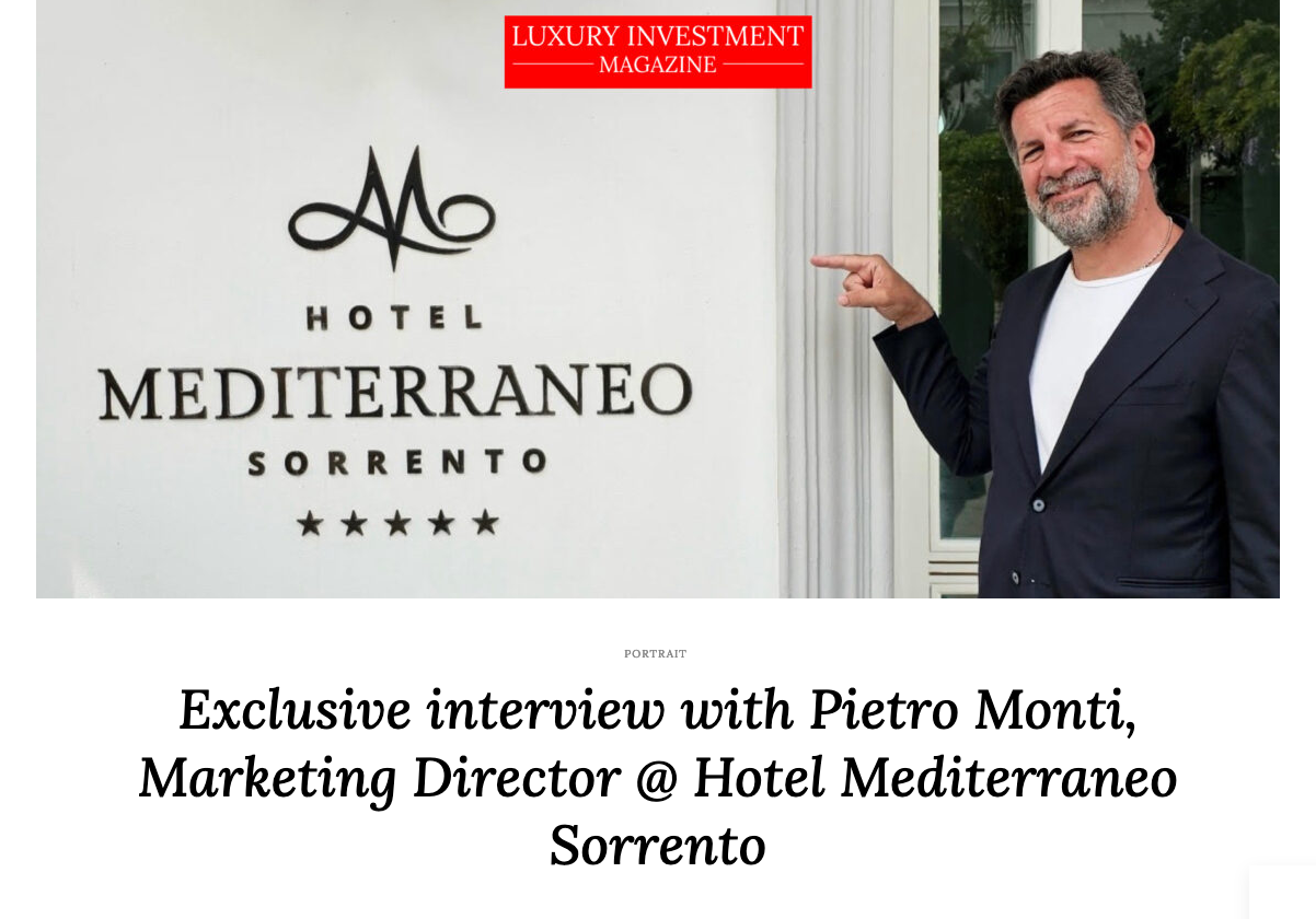 Pietro Monti, Marketing Director at Hotel Mediterraneo Sorrento, pointing toward the hotel's logo and name on a wall.