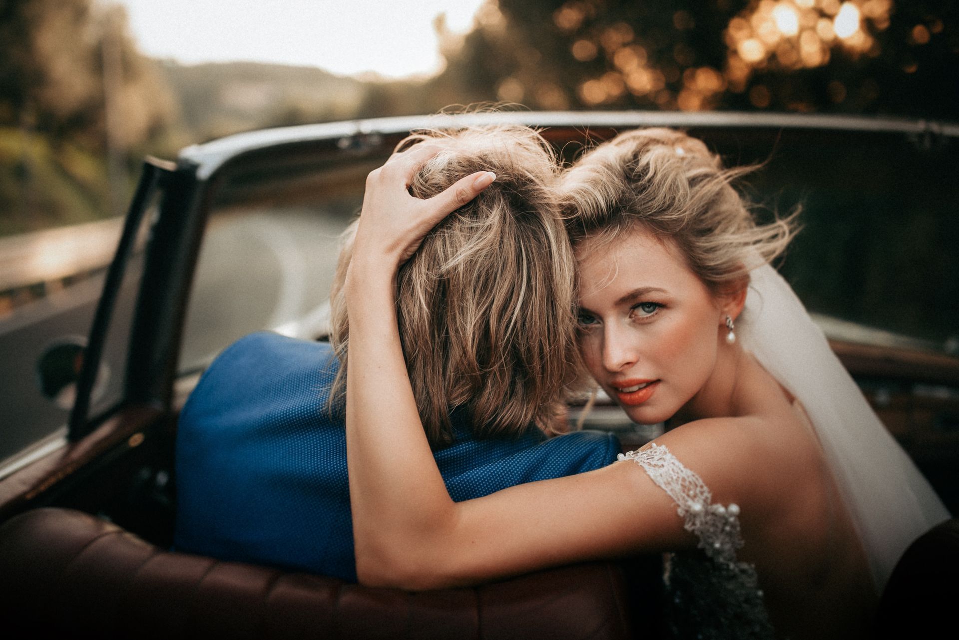 Couple embracing in a vintage car, with the bride gazing at the camera.