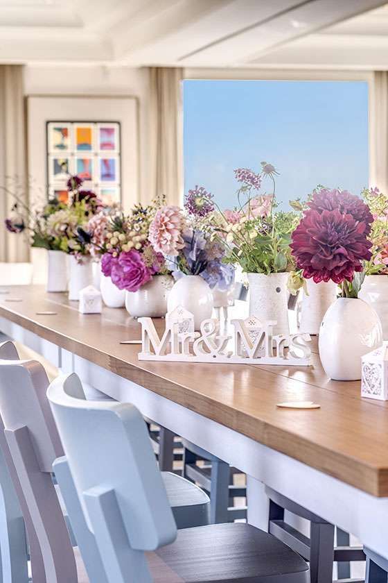 A long table featuring white vases filled with colorful flower bouquets and a 