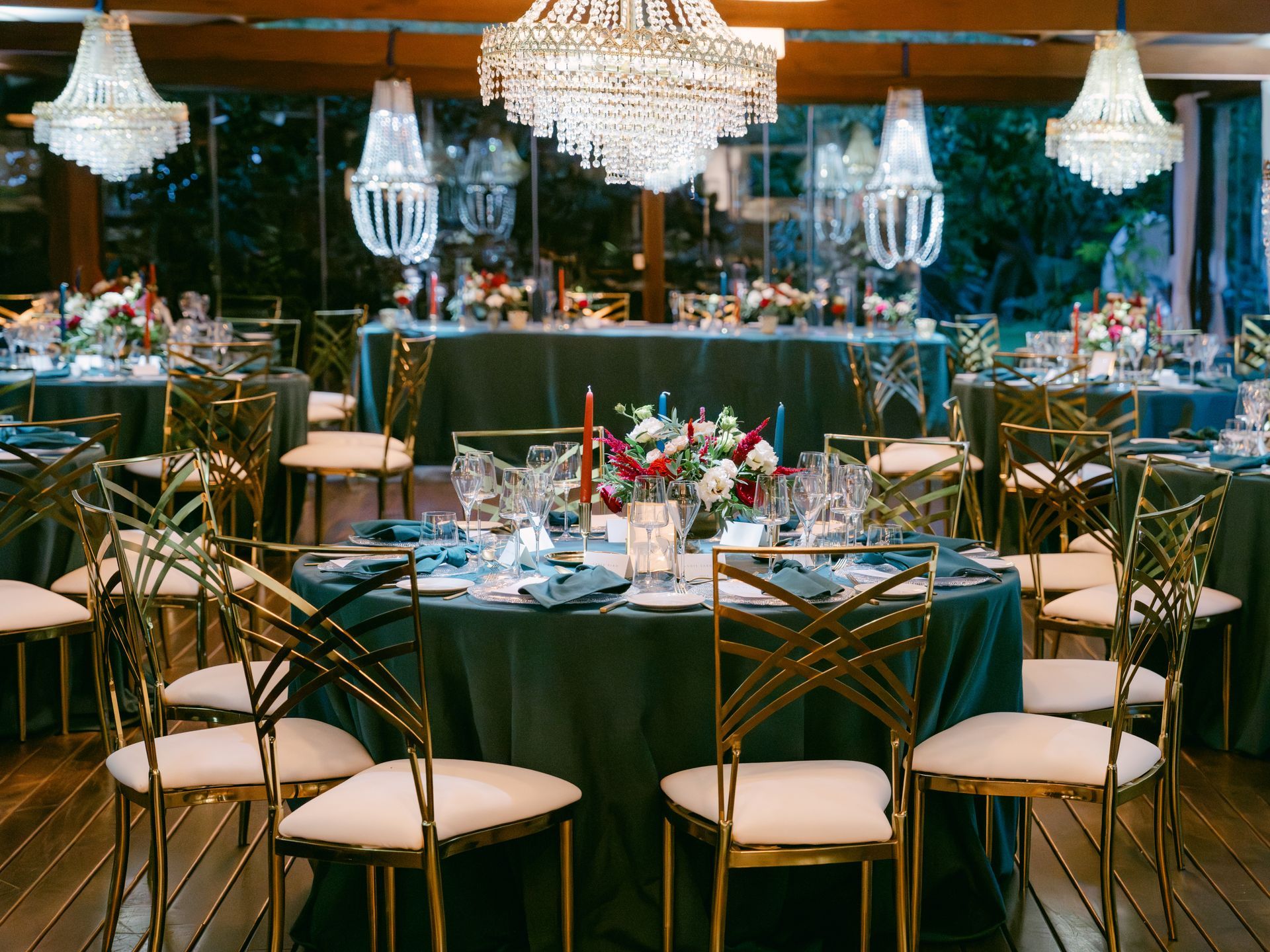 Formal event setting with dark green tablecloths, ornate gold chairs, crystal chandeliers, and floral centerpieces.