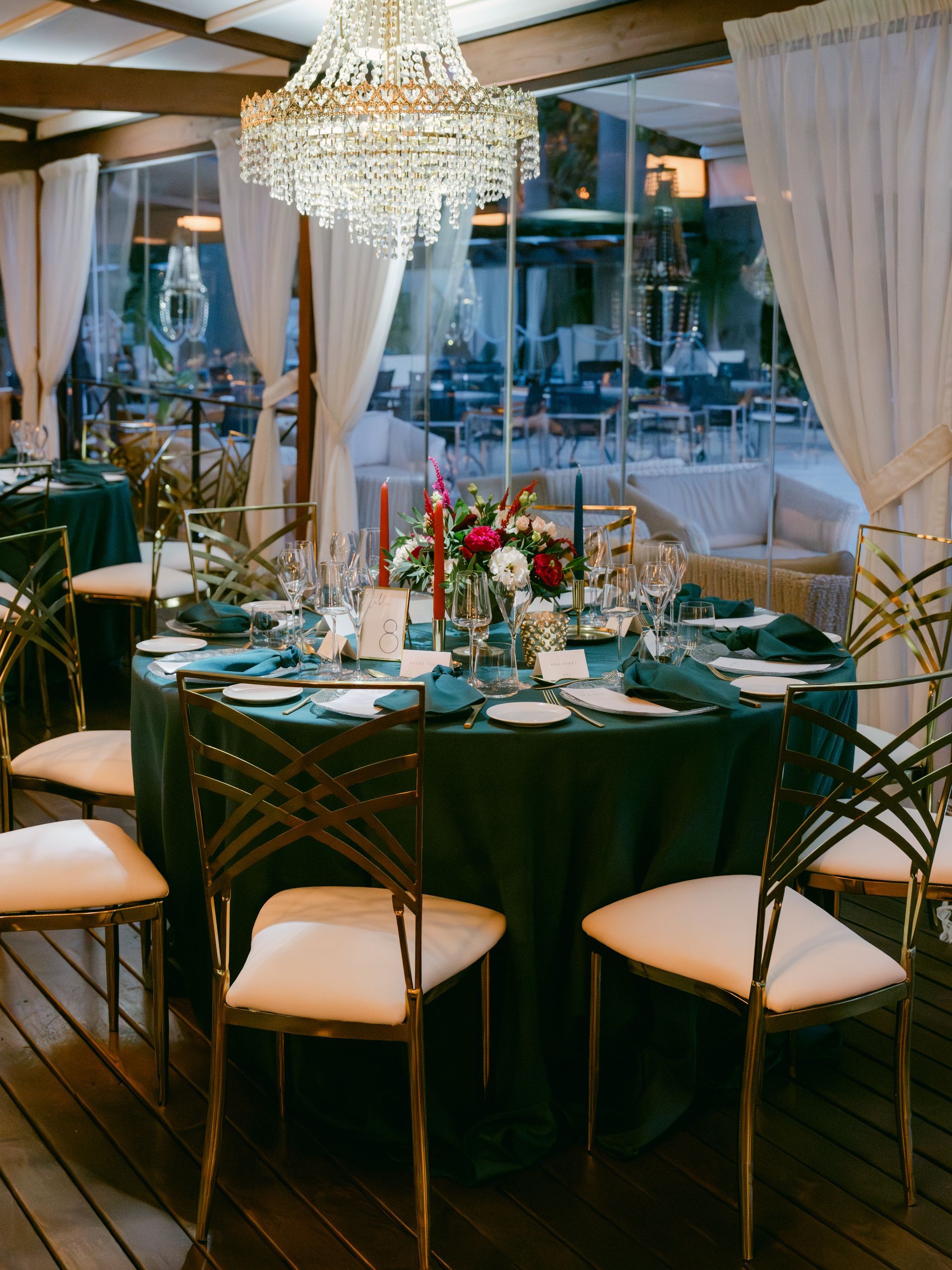 A dining table with a dark green tablecloth, floral centerpieces, and ornate gold chairs under a crystal chandelier.