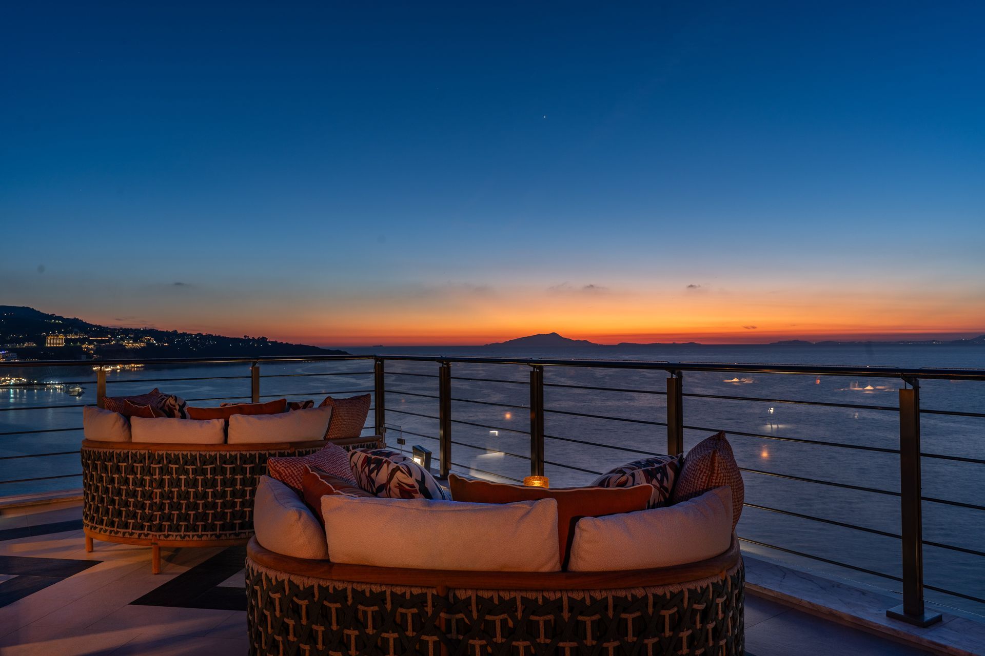 Terrazza panoramica sul tetto con divani curvi che si affaccia sul mare al tramonto.