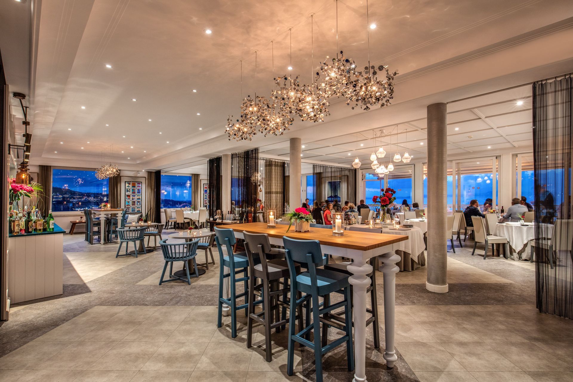 Gli interni spaziosi ed eleganti di questo ristorante sono caratterizzati da tavoli alti con sgabelli blu, lampadari decorativi e una splendida vista.