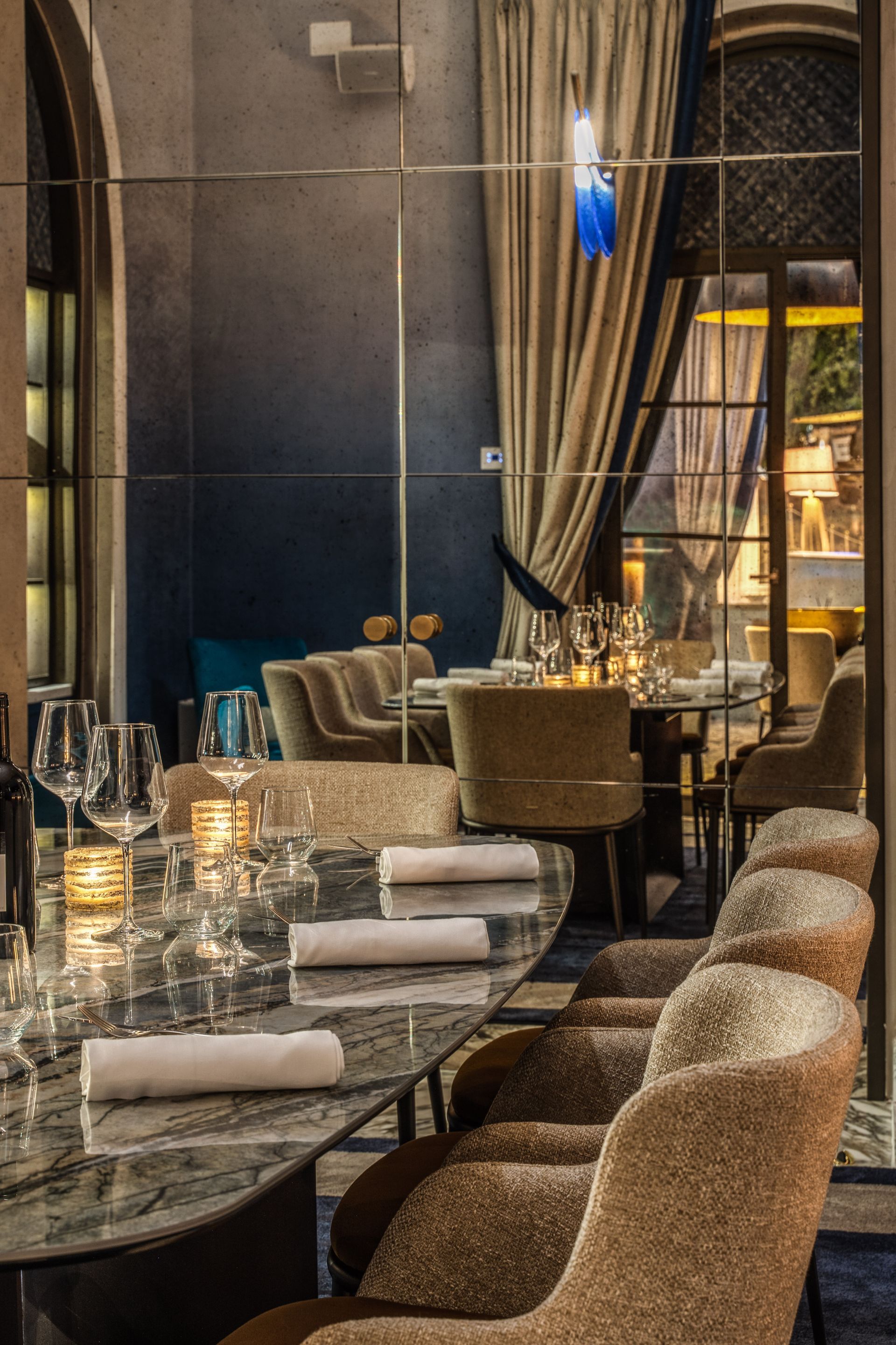 Un'elegante sala da pranzo con un lungo tavolo in marmo, poltrone con finiture di pregio e pannelli a specchio a tutta altezza con illuminazione soffusa.