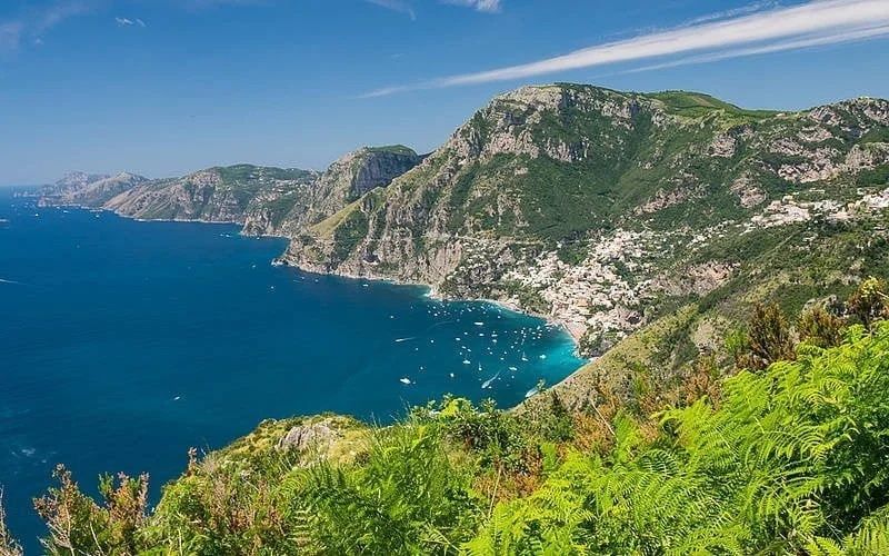 A coastal view of Positano, Italy, featuring colorful buildings nestled on steep cliffs above a blue sea filled with boats.