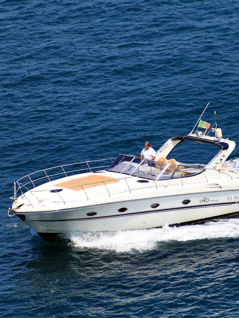 Un motoscafo bianco con la bandiera italiana che solca le acque blu intenso dell'oceano.