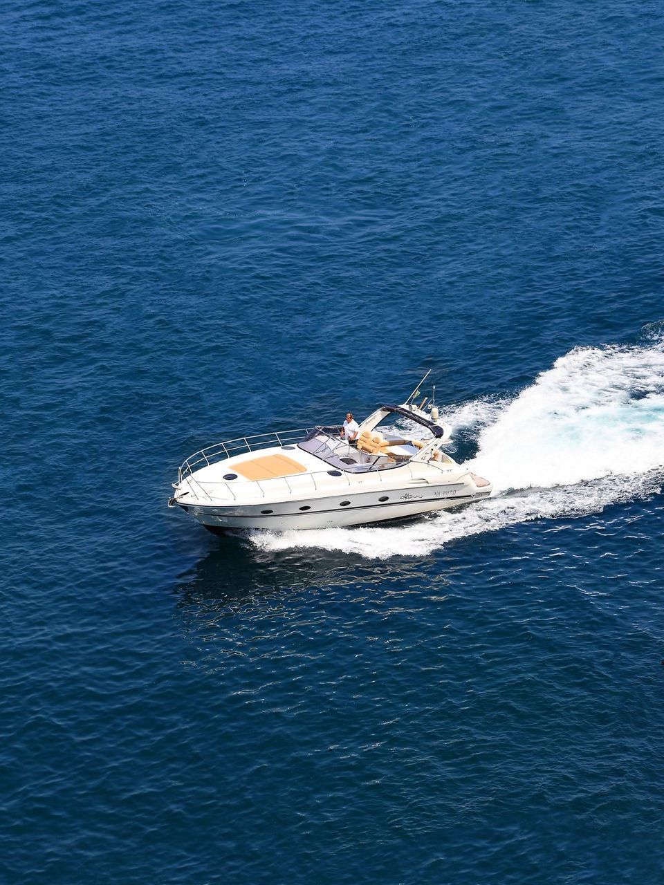 A white motorboat cruising through deep blue water, creating a white wake behind it.