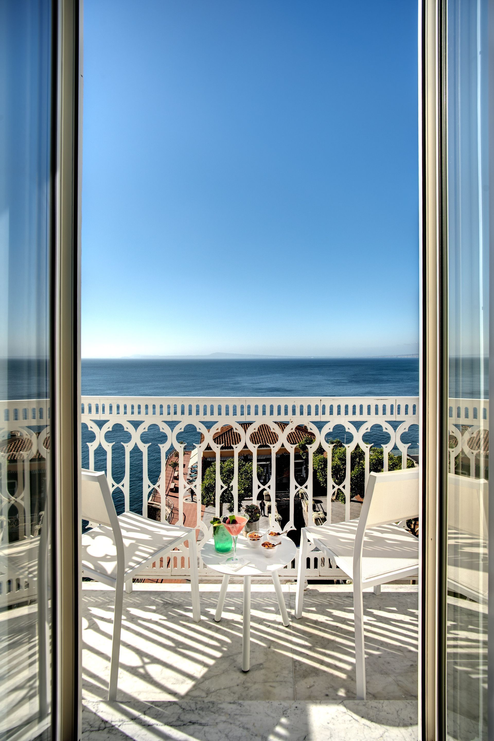A balcony with two white chairs and a small table overlooking the sea under a clear blue sky.
