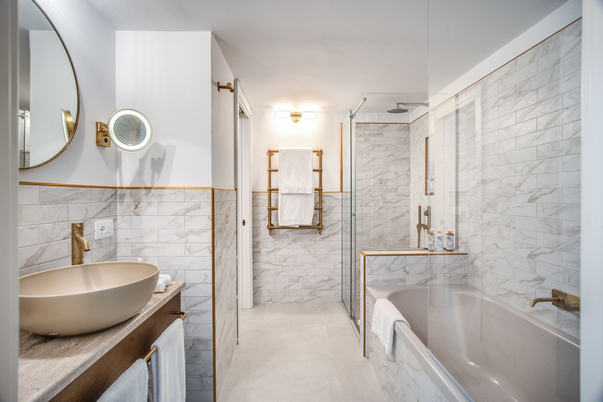 Bagno moderno con lavabo a ciotola di colore chiaro, piastrelle effetto marmo, vasca da bagno e box doccia in vetro.