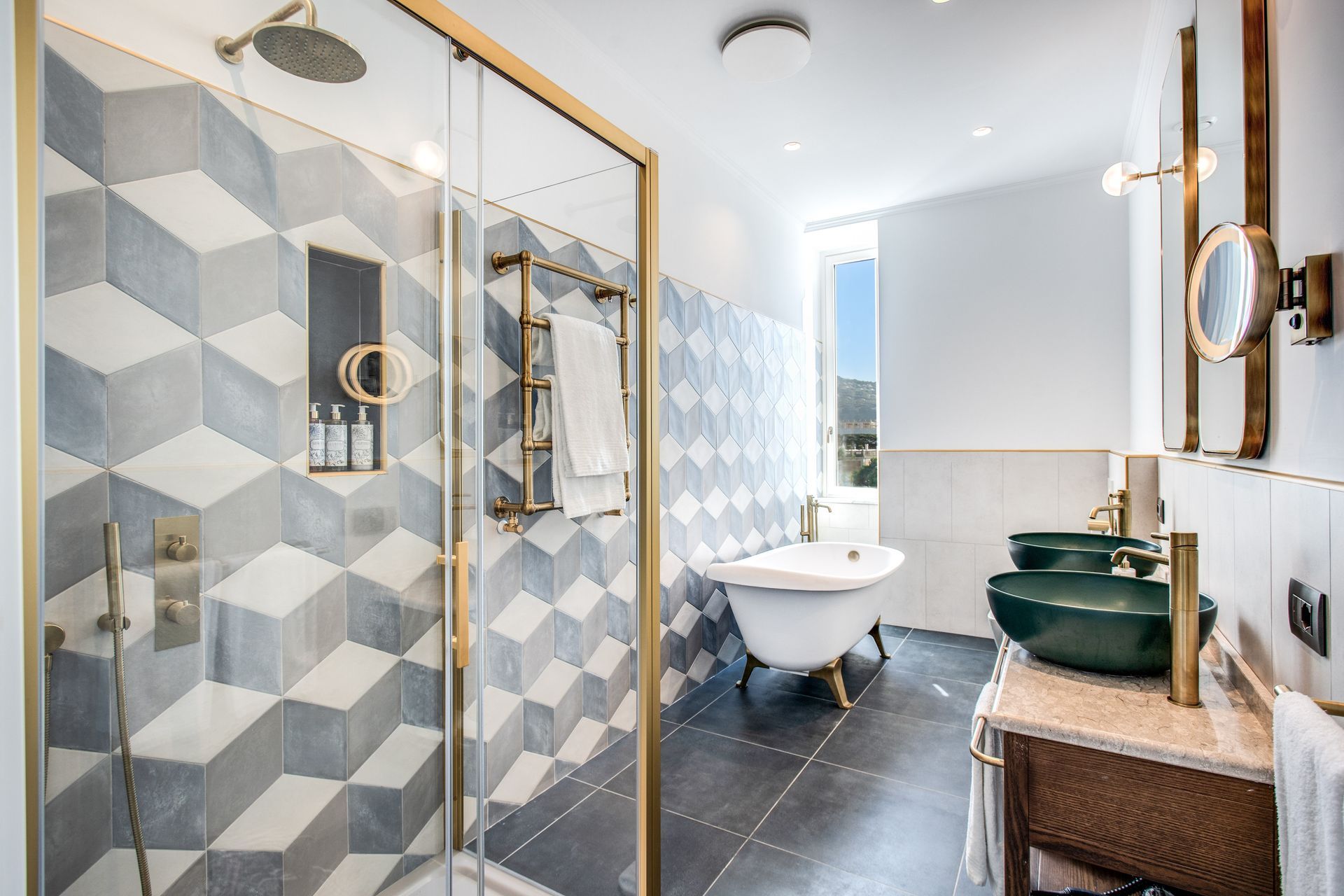 Bagno moderno con doccia con box in vetro, pareti rivestite con piastrelle geometriche, vasca freestanding con piedini e mobile lavabo con lavandino.