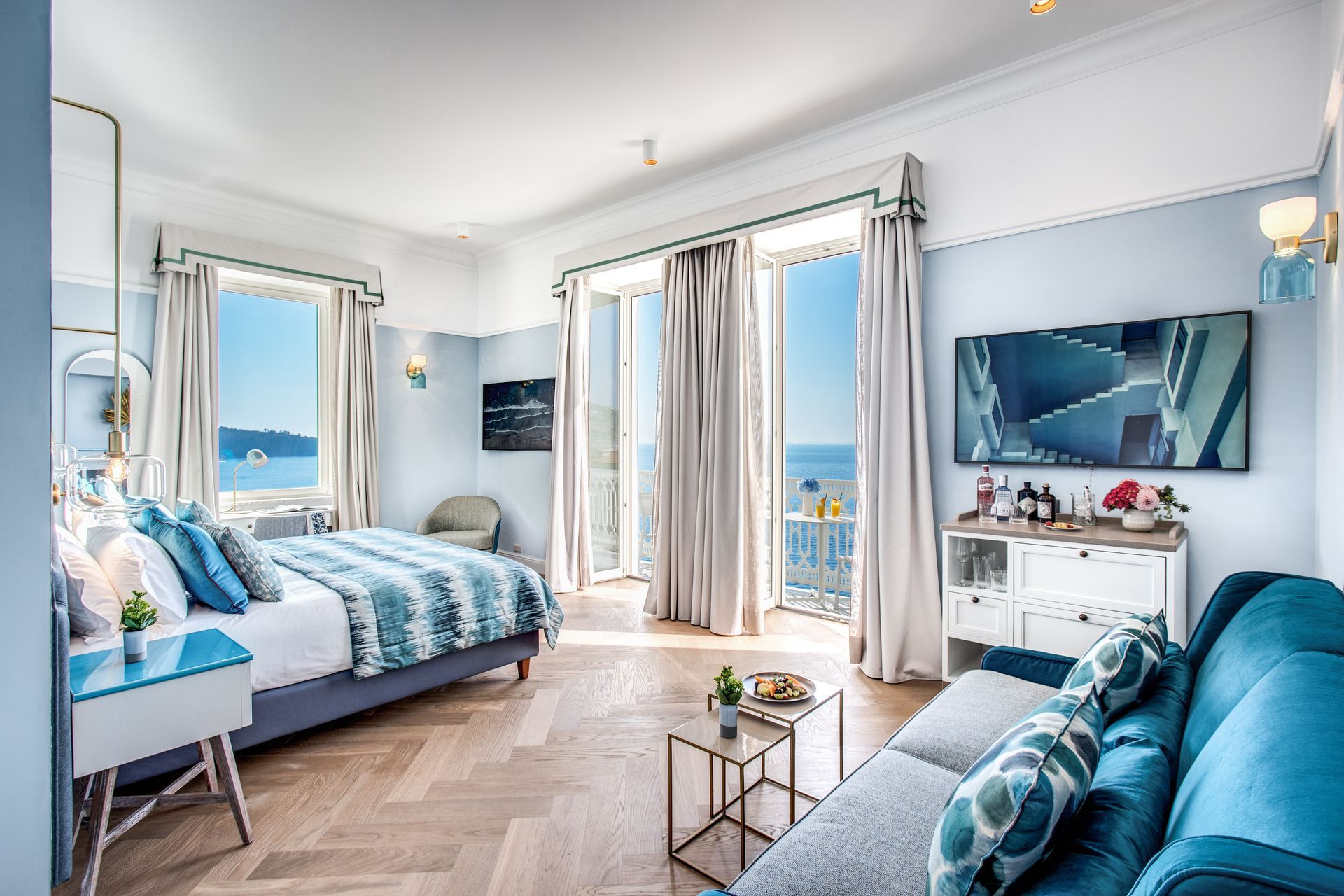 Bright hotel room with a sea view, featuring a king bed, blue patterned accents, wood floors, and a sofa.