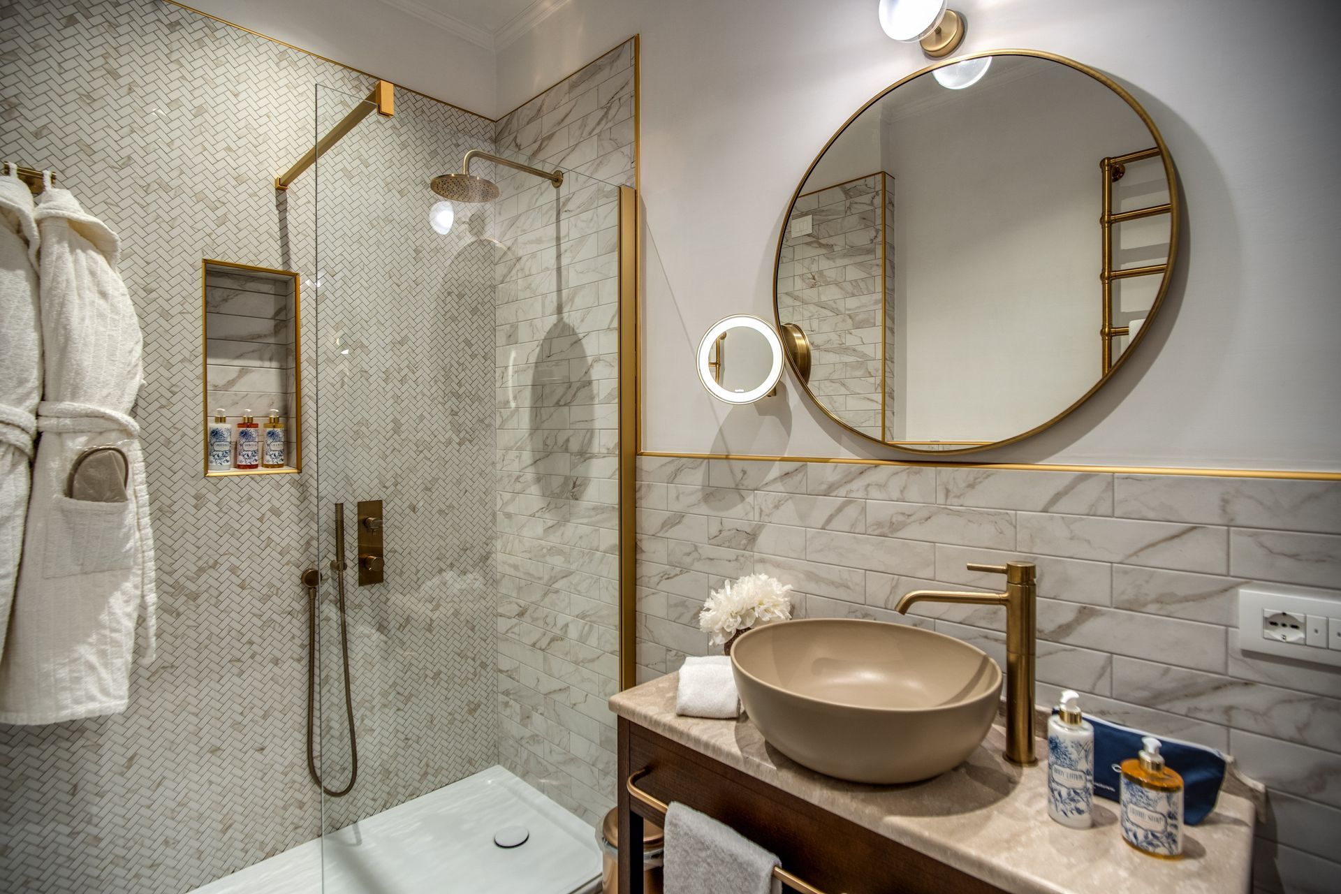 Un bagno moderno con doccia in vetro, specchio rotondo e lavabo a ciotola con rubinetteria dorata.