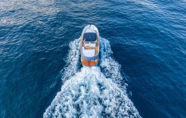 Aerial view of a small motorboat moving through deep blue water, leaving a wide white wake behind it.
