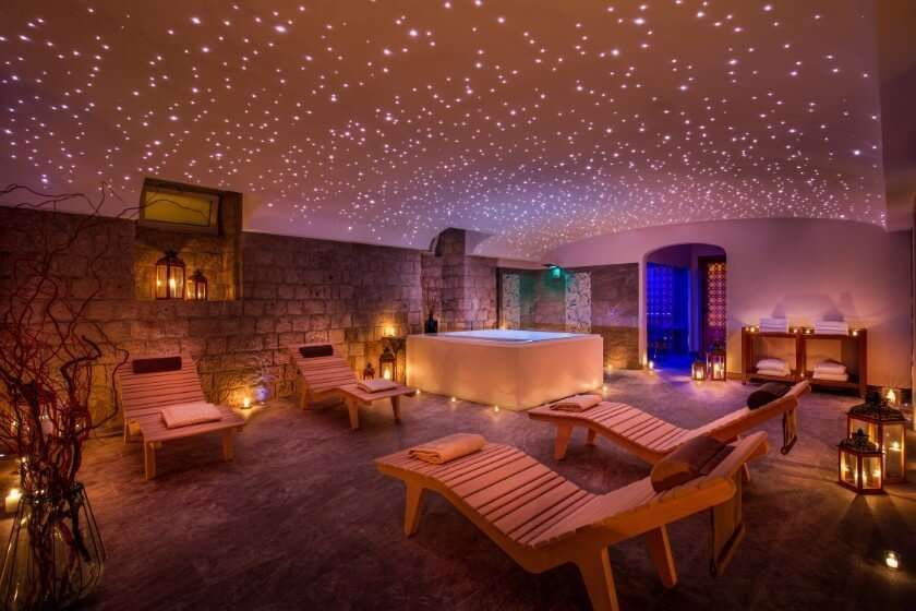 A relaxing spa room with wooden lounge chairs, a central hot tub, and a starry night light effect on the ceiling.