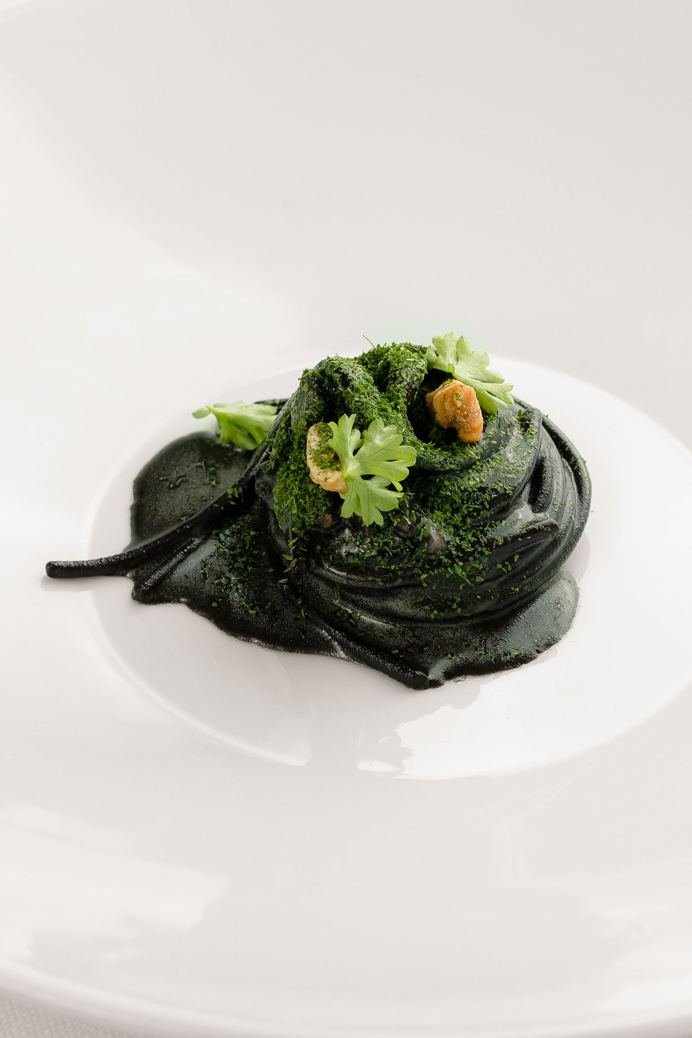 Una porzione di pasta verde scuro o di purea mescolata in una ciotola, guarnita con un rametto di coriandolo fresco e piccoli pezzetti dorati.