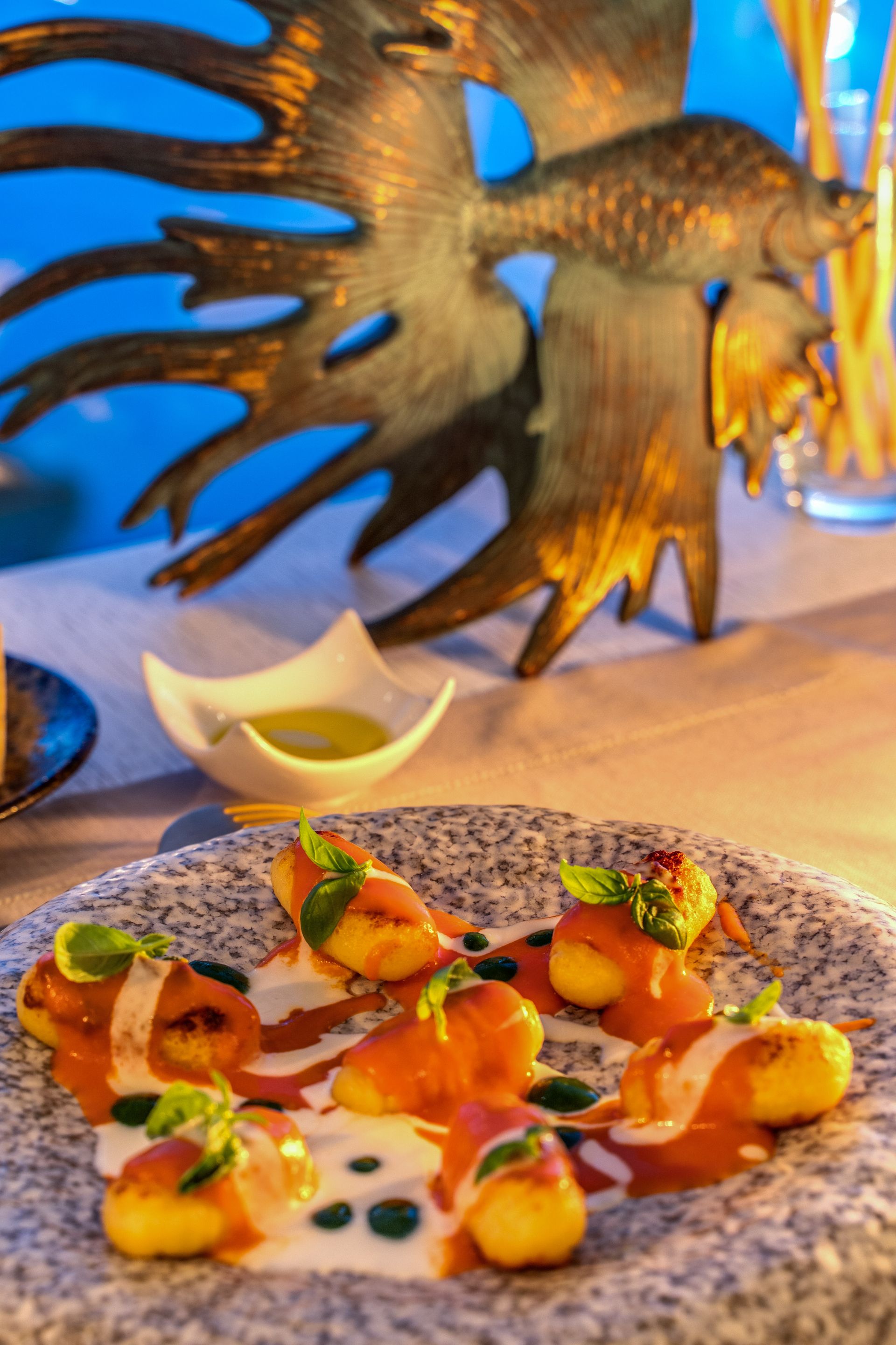 A plate of gnocchi with red sauce and cream, garnished with basil, in front of a decorative gold fish sculpture.