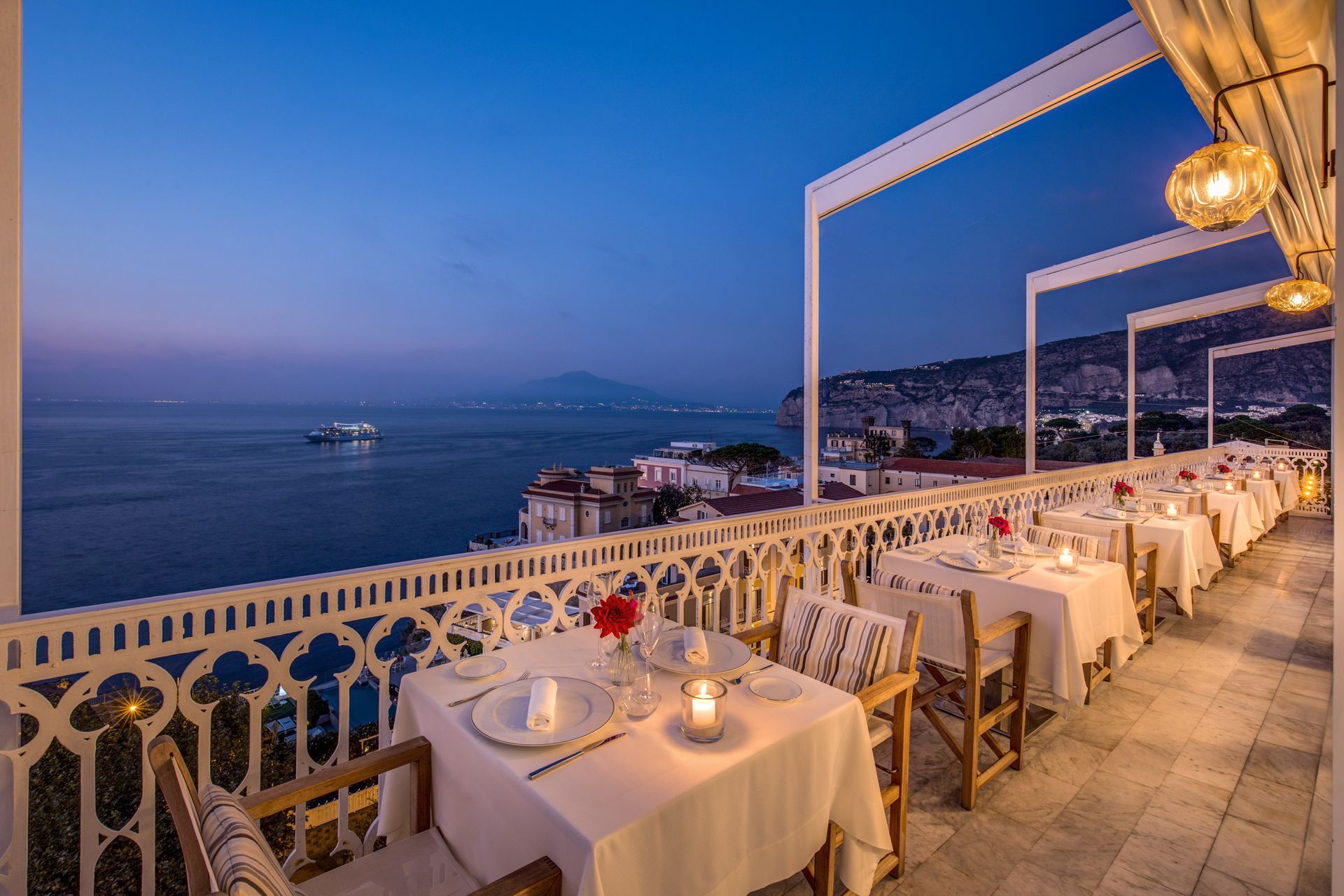 Outdoor restaurant terrace with tables set for dinner overlooking the ocean at twilight.