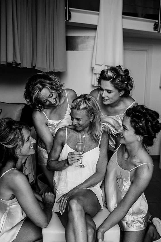 Five individuals in matching loungewear smile and chat while holding a glass in a brightly lit indoor space.