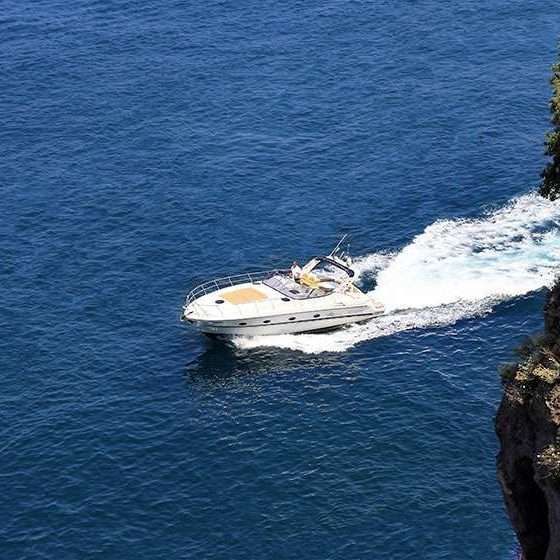 Un motoscafo bianco solca le acque blu intenso, lasciando una scia bianca dietro di sé vicino a una scogliera rocciosa.