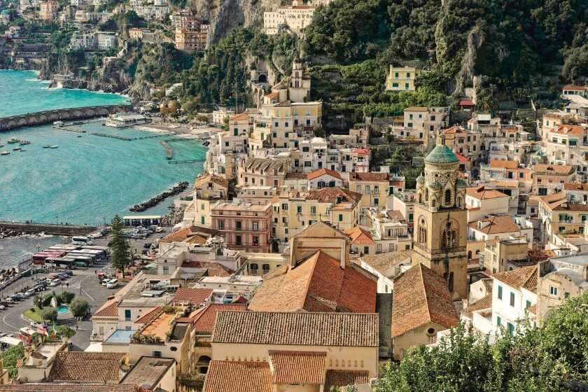 A picturesque Italian coastal village with colorful houses, a church bell tower, and a harbor on the Tyrrhenian Sea.