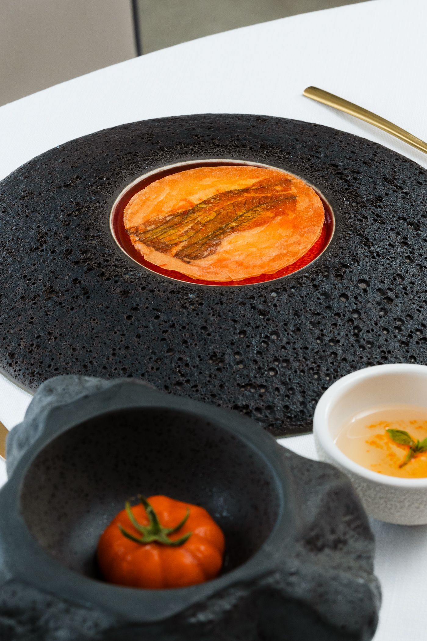 Un piatto raffinato presenta una crostata circolare all'arancia su un piatto nero dalla superficie ruvida, con una ciotolina di pomodori e una di salsa a lato.