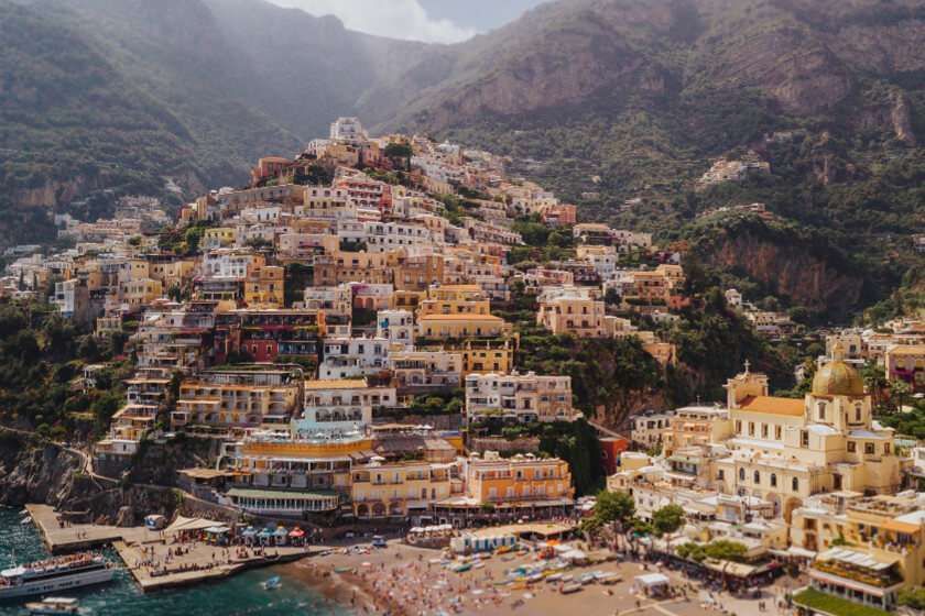 Una cittadina collinare in Italia, caratterizzata da edifici colorati che digradano dolcemente verso la spiaggia e il mare, con una cupola della chiesa ben visibile.