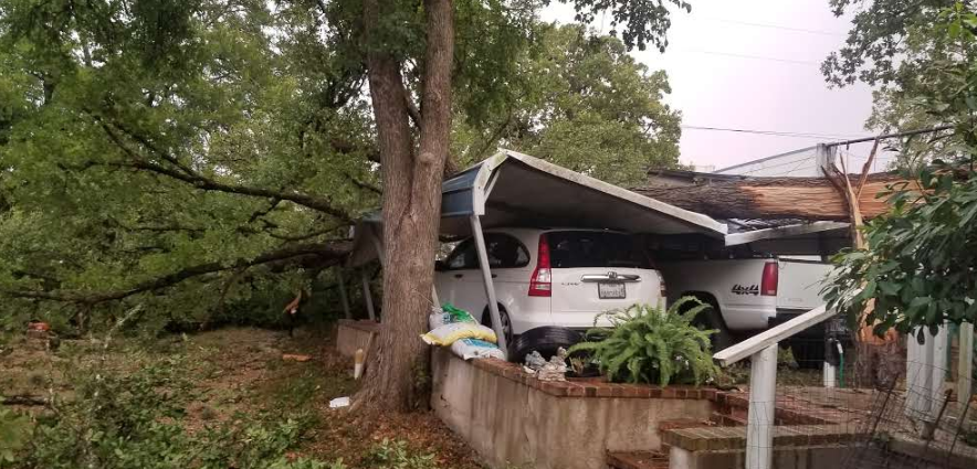 A car is parked under a carport that has been damaged by a tree.