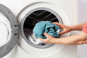 A person is putting a blue towel into a washing machine.