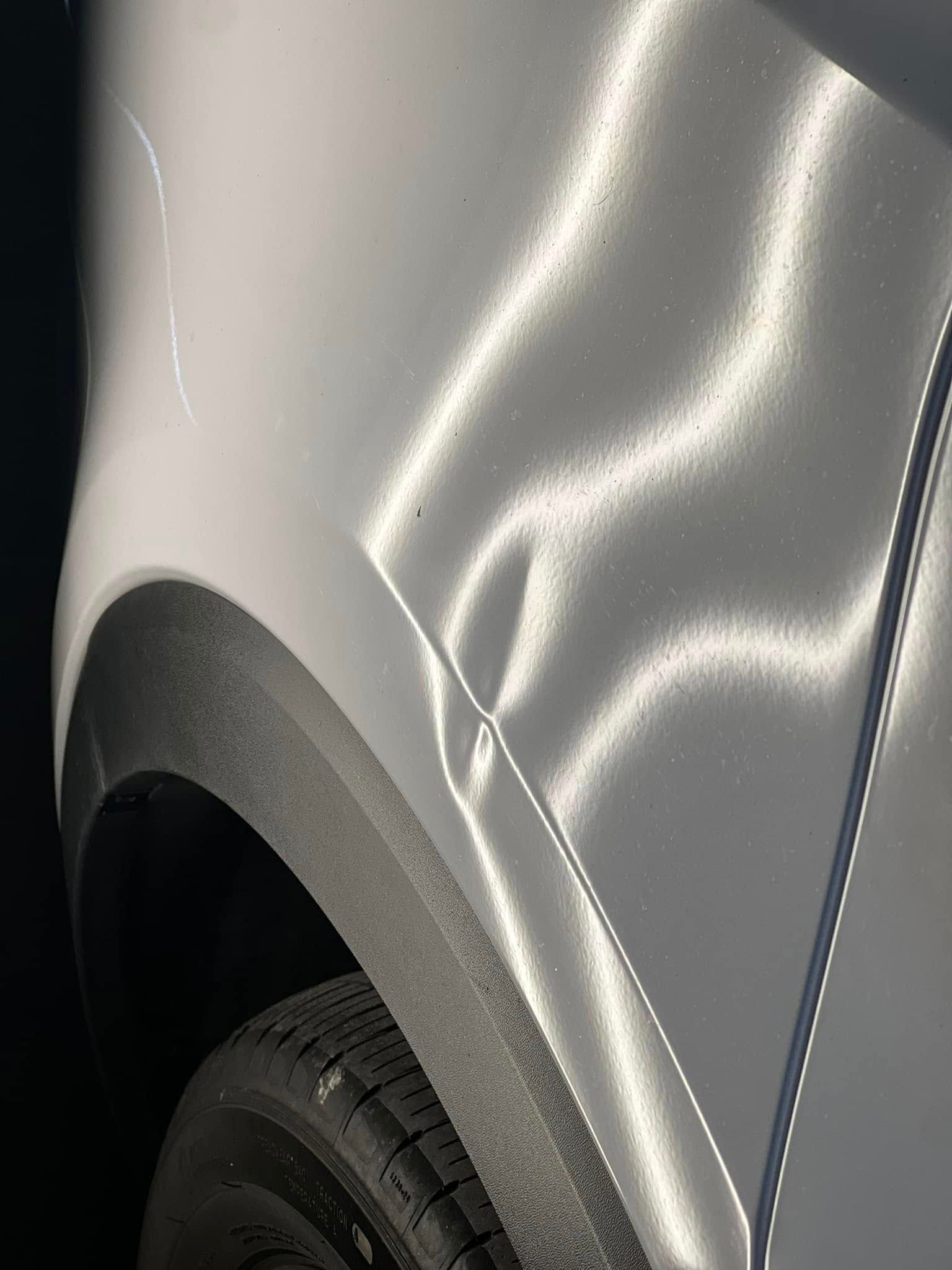 A white car fender with a dent above the wheel well reflecting light.