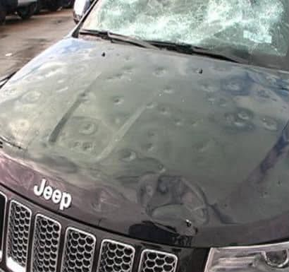 Black Jeep SUV with extensive hail damage on hood and windshield.