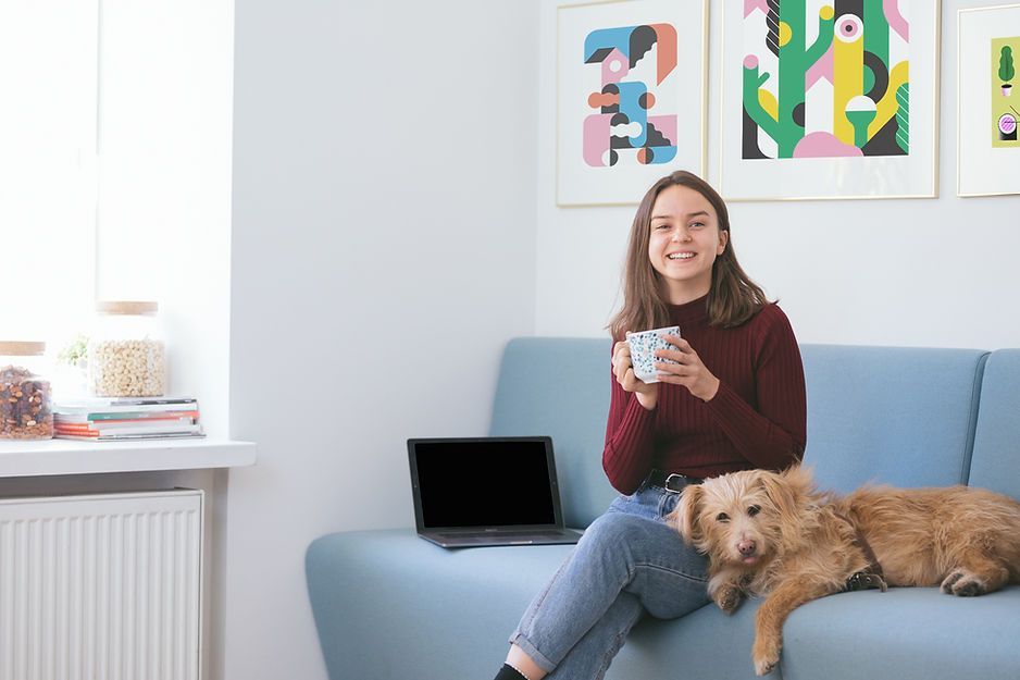 A woman is sitting on a couch with a dog and a laptop.