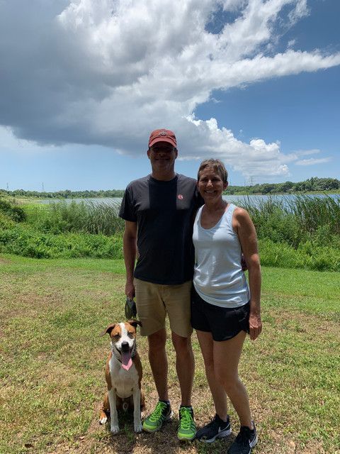 A man and a woman are standing next to a dog in a field.