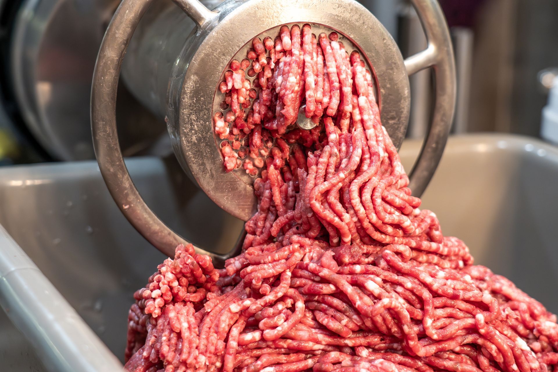 Ground meat being extruded from a meat grinder into a metal bin.