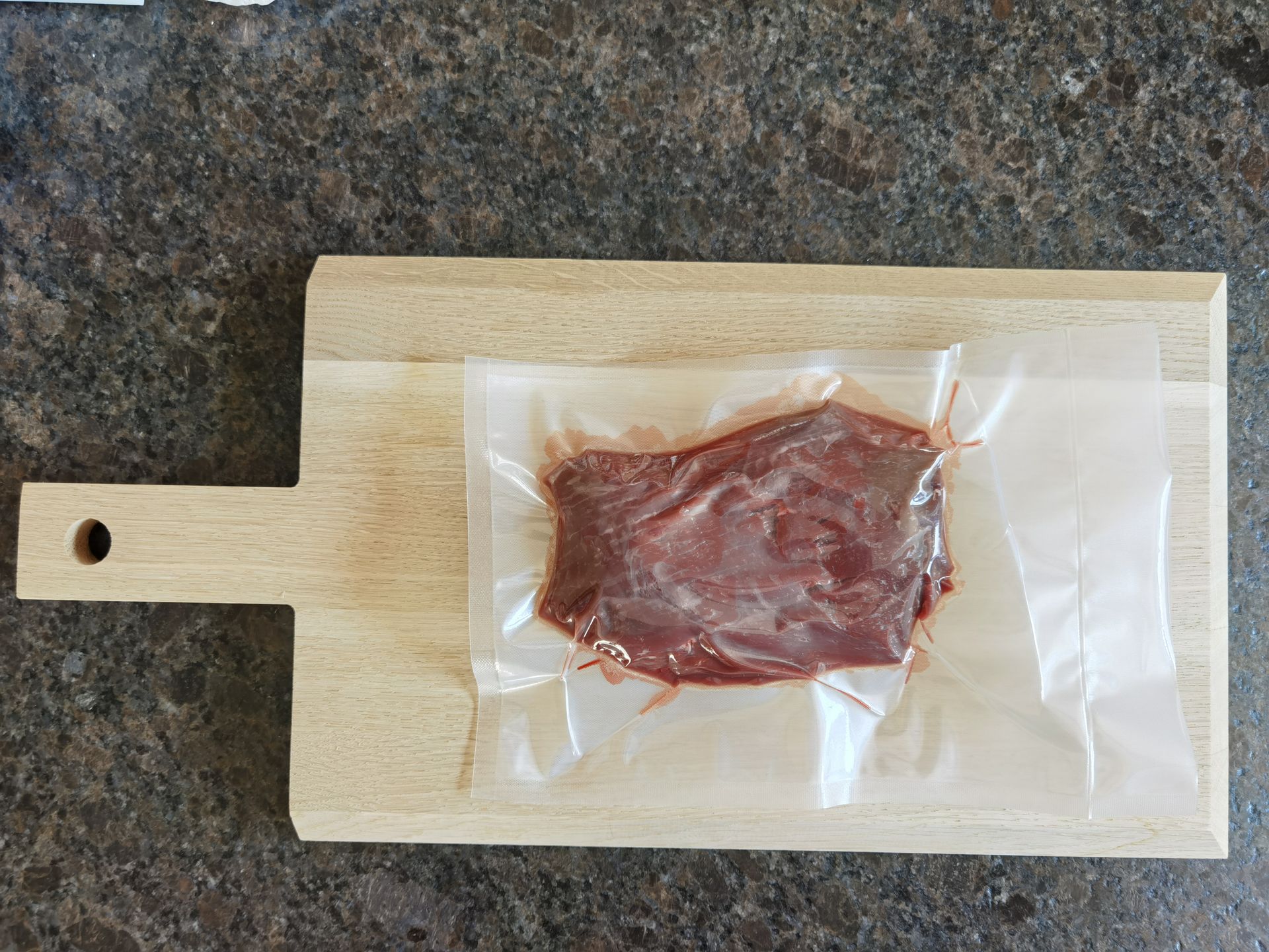 Vacuum-sealed, raw red meat on a light wooden cutting board.