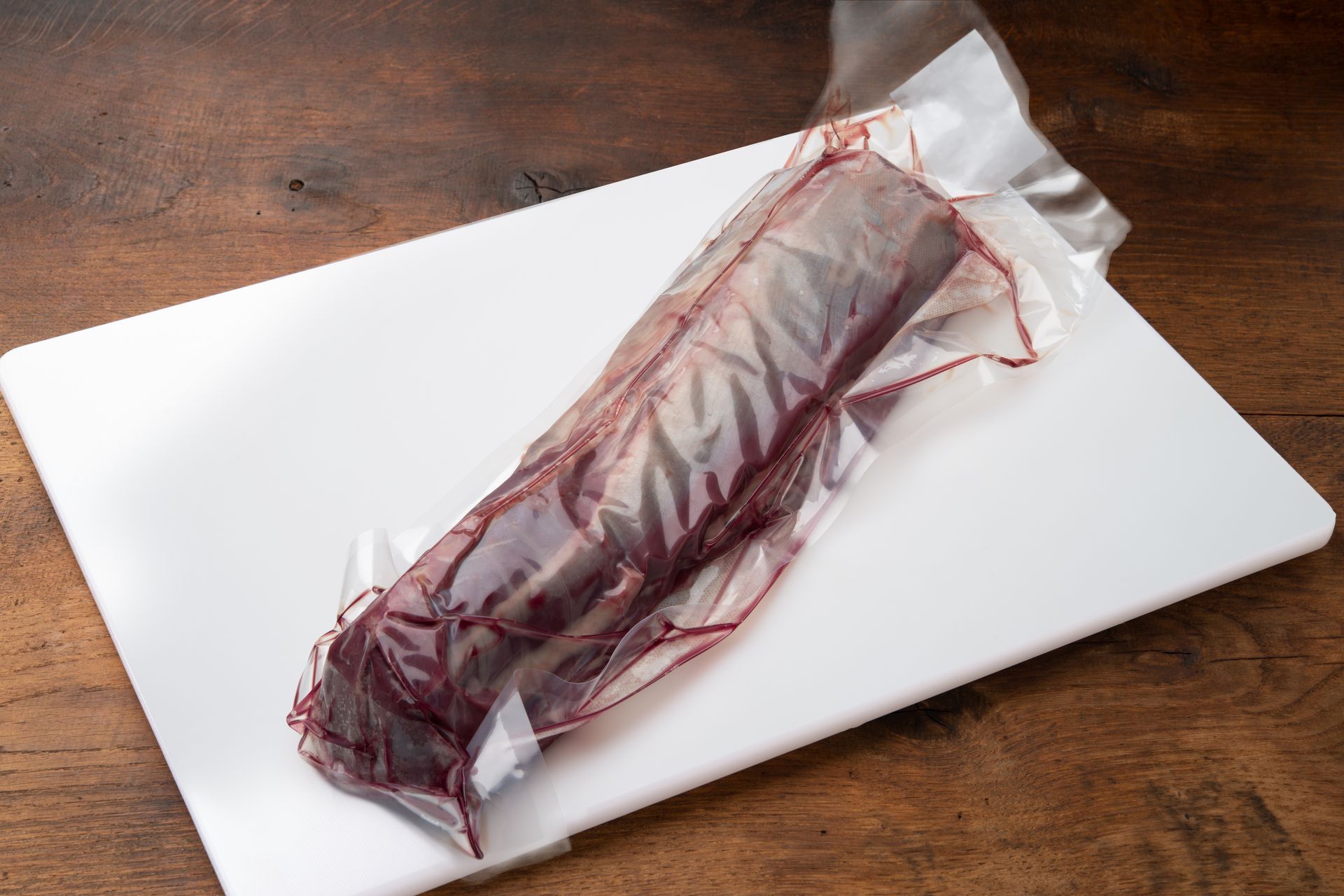Vacuum-sealed raw meat on a white cutting board, set on a wooden surface.