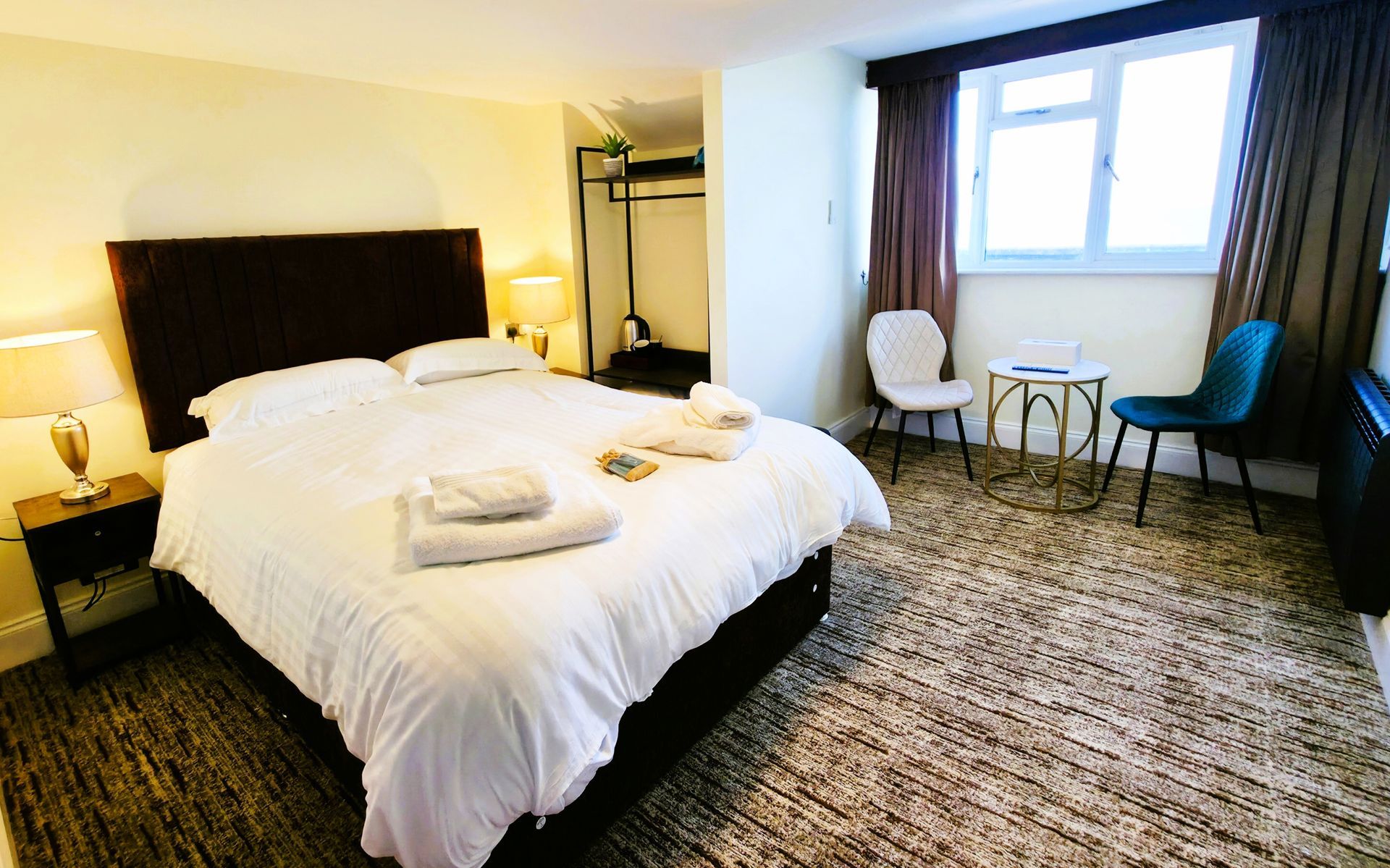 Bedroom with double bed, window with ocean view, brown curtains, and a nightstand with a lamp.