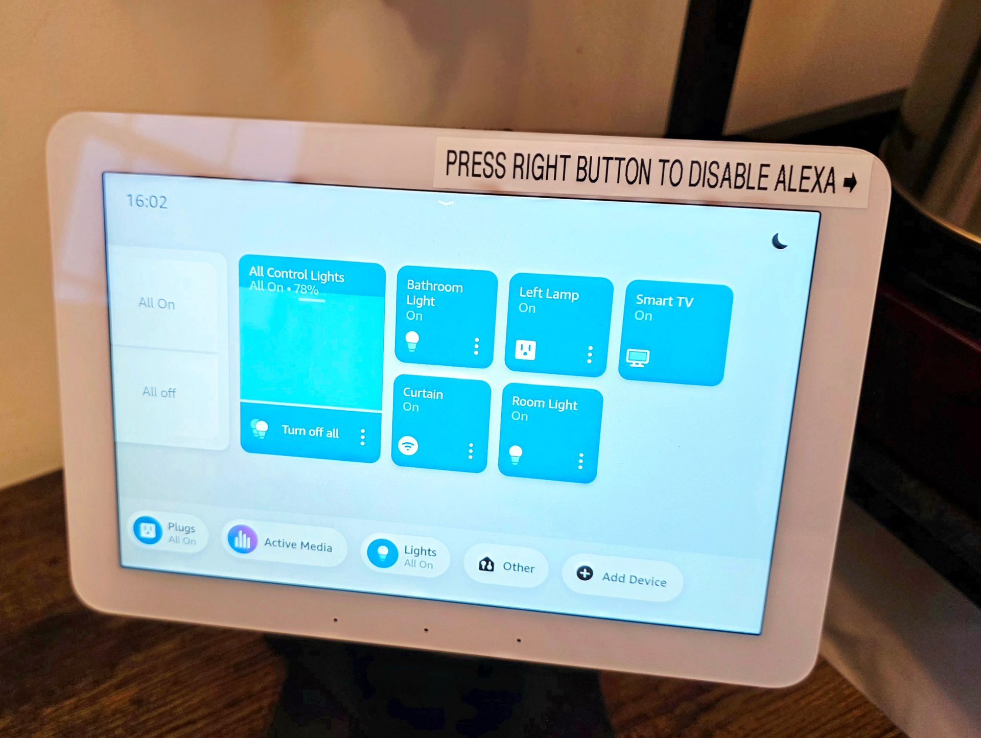 A white smart home tablet displaying app icons on a wooden surface with a label: 