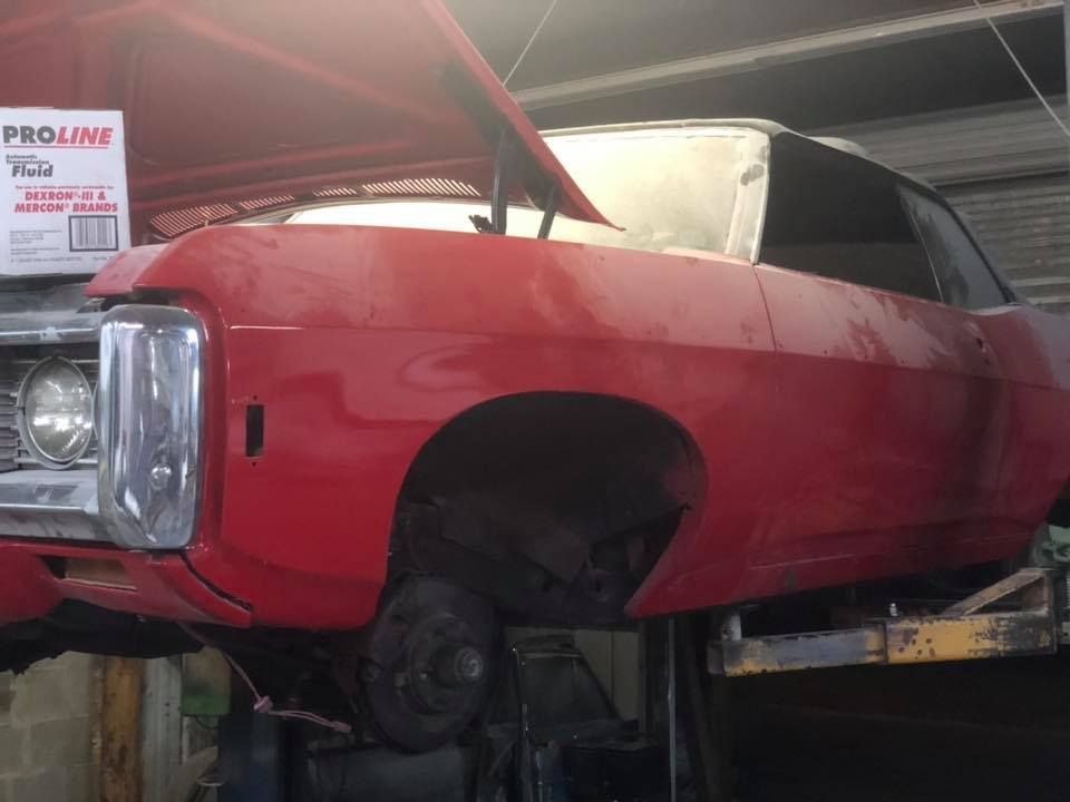 Red classic car on a lift with the hood open, revealing engine parts.