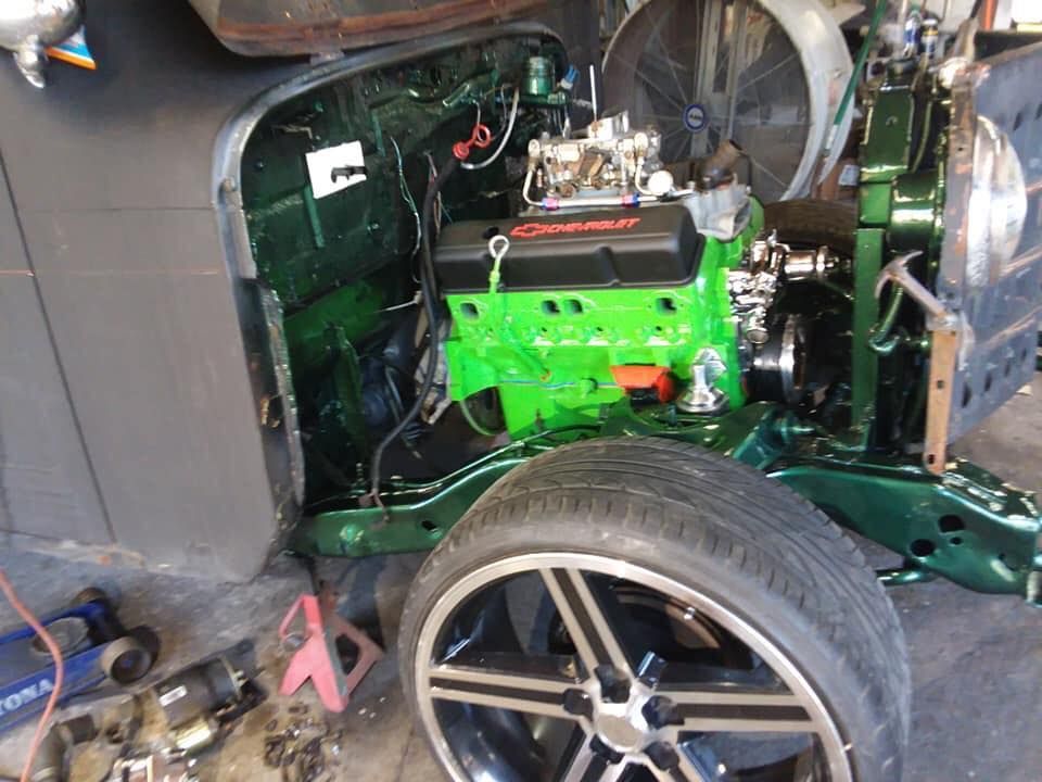 Green engine in a truck engine bay, wheel visible, workshop setting.