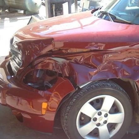 Damaged maroon car front, crumpled hood and fender, tire visible.