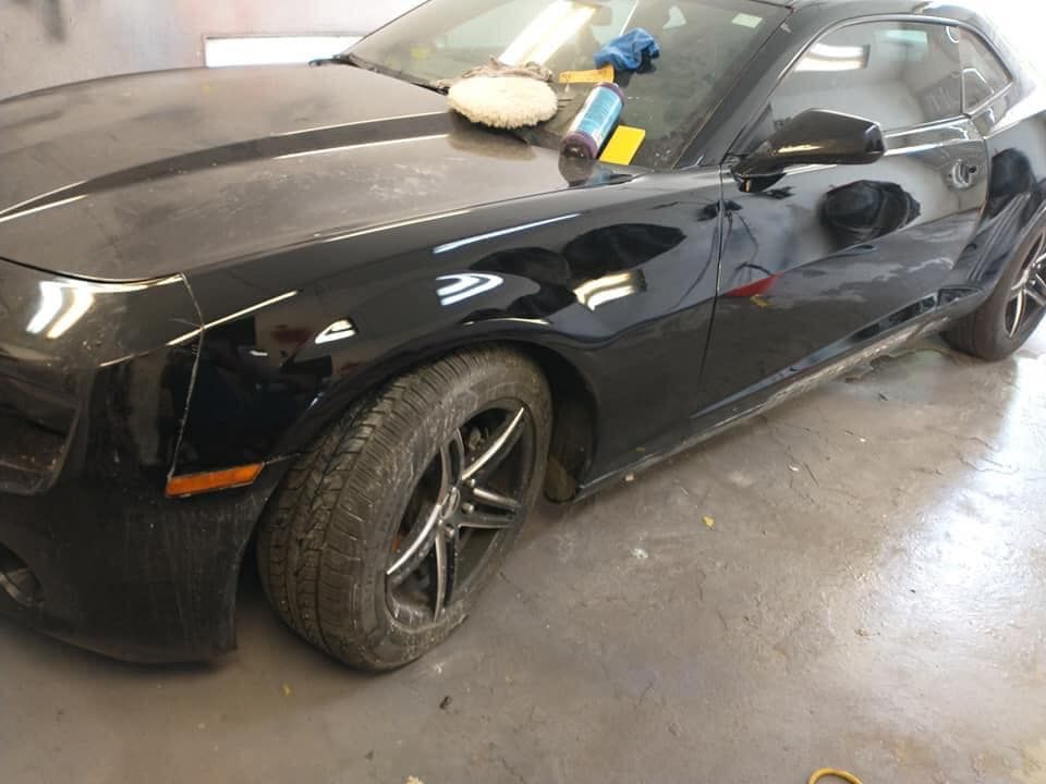 Black Camaro car in a garage, possibly undergoing repairs. It has a dirty tire and some tools on the hood.