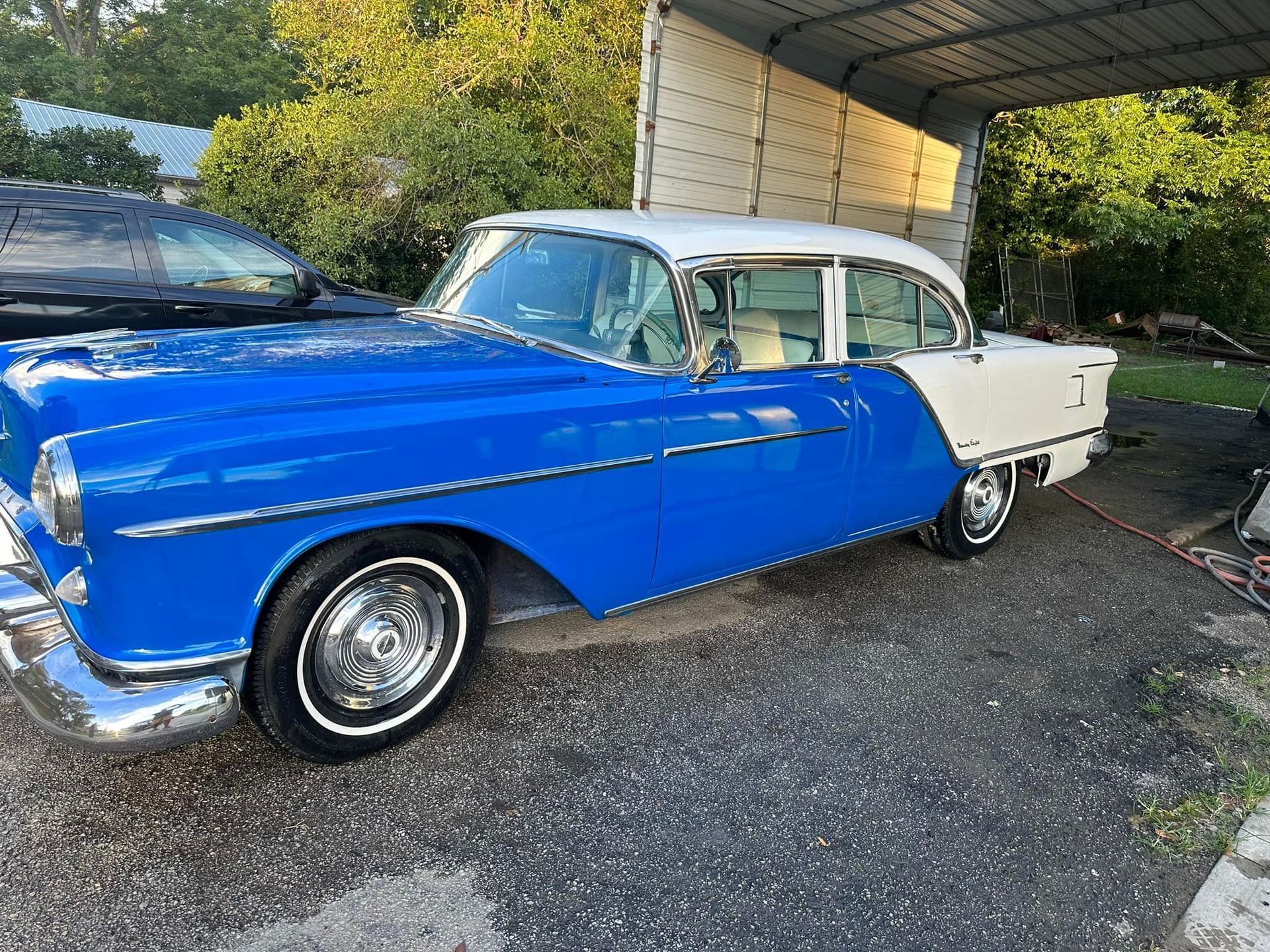 Blue and white classic car parked under a carport.