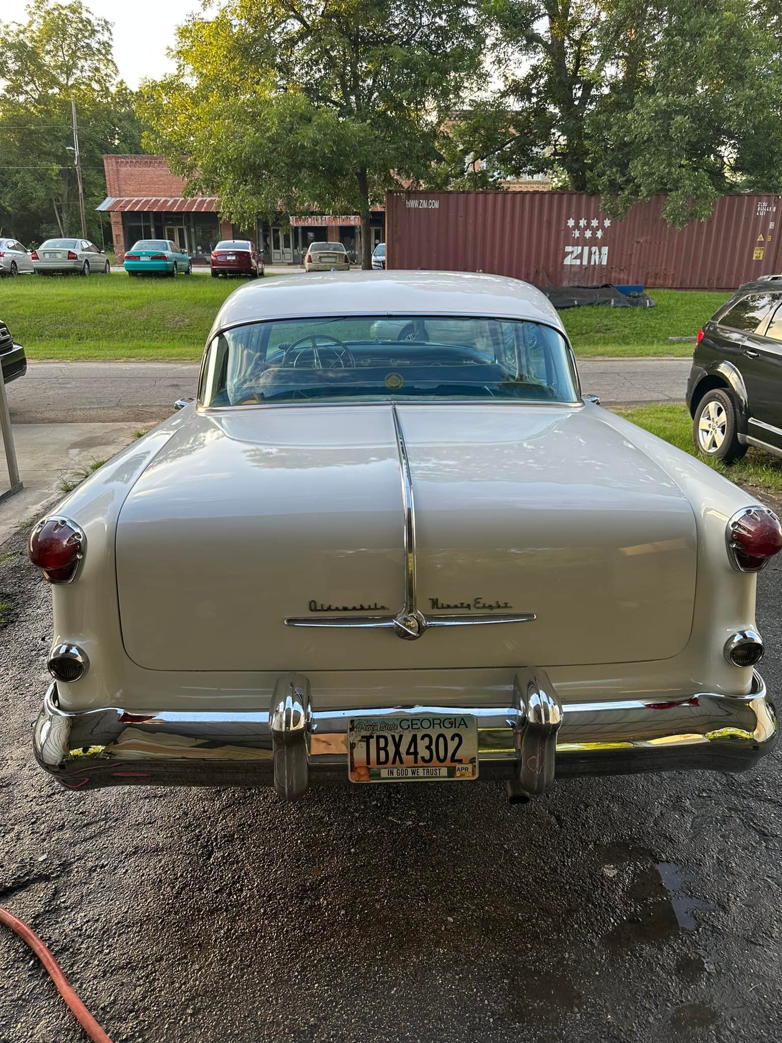 Rear view of a light beige classic car with chrome accents, license plate, and taillights, parked outside a building.